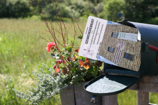 Briefkasten auf einer Wiese, aus dem der Gemeindebrief rausschaut